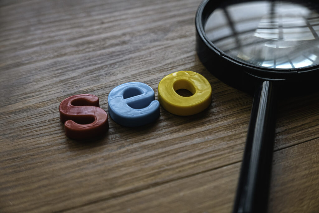 Colorful letters spelling "seo" on a wooden surface next to a magnifying glass