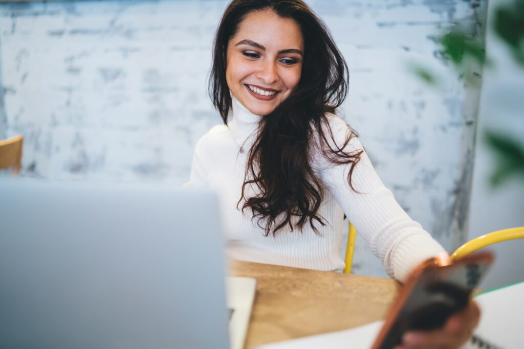 Cheerful woman 20s browsing wireless website during networking via smartphone device